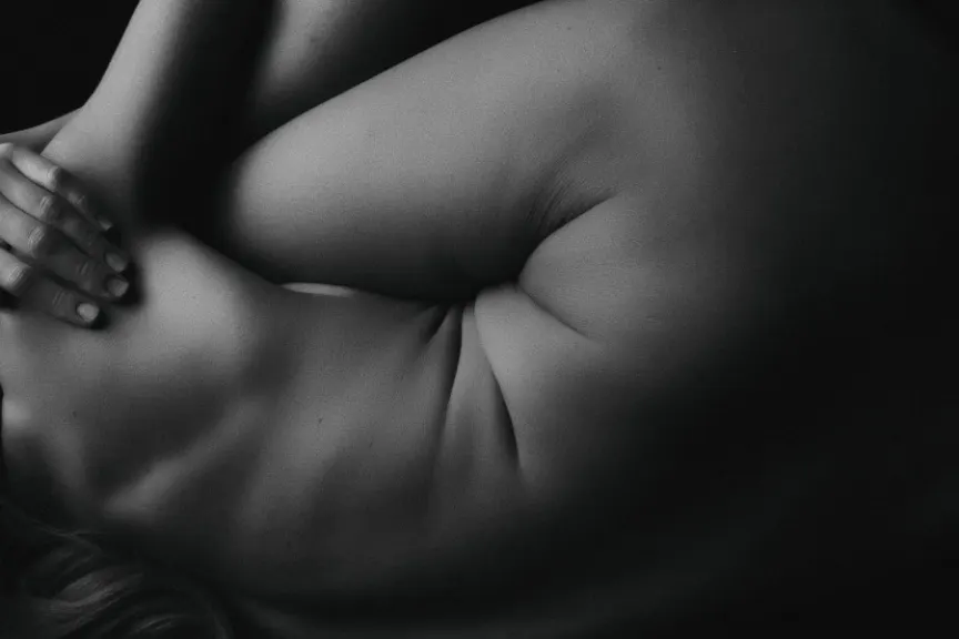 黑白照片中的女性蜷缩着身体，展示了自己的腹部