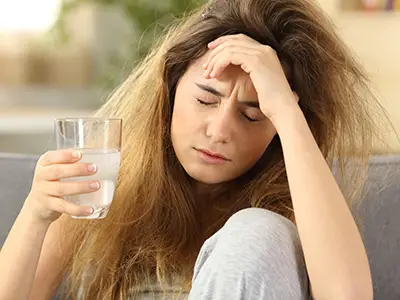 Young woman with headache drinking a glass of water.
