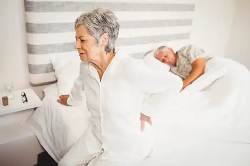 Senior woman suffering from a backache sitting on a bed in a bedroom