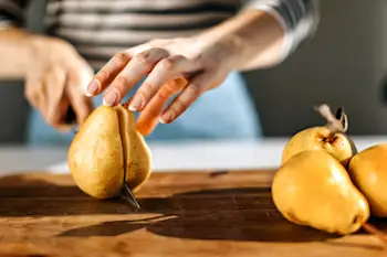 Closeup of a woman cutting a pear on a cutting board.