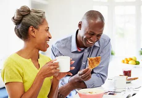 Un hombre y una mujer ríen mientras desayunan una tostada y un café