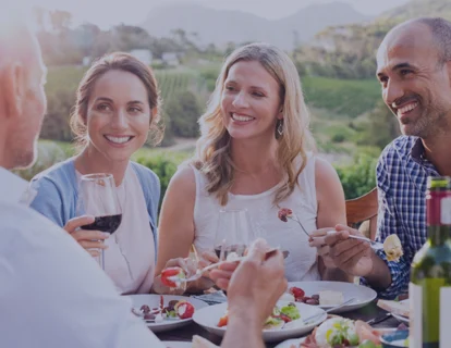 Un grupo de amigos comiendo y bebiendo en un viñedo, están sonriendo y uno de ellos lleva una prótesis parcial. Se siente seguro ya que conoce los diferentes tipos de prótesis parciales y utiliza Kukident.