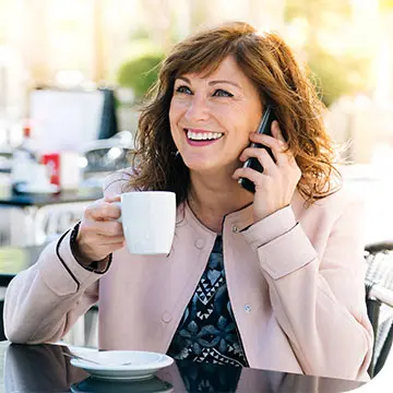 Mujer de mediana edad sonríe mientras habla por teléfono y sujeta una taza de café