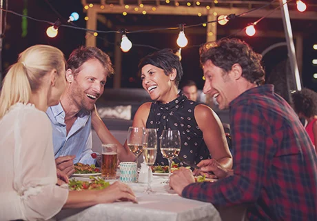 Un grupo de amigos sentados alrededor de una mesa cenado, tomando algo y hablando de prótesis dentales fijas.