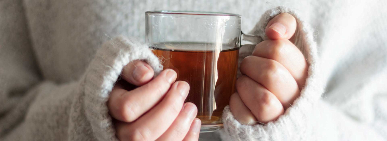 Woman in woolen sweater holding a hot cup of tea