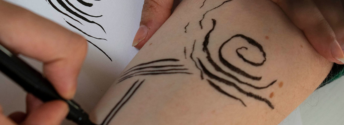 Close-up of hands making a drawing on an arm.