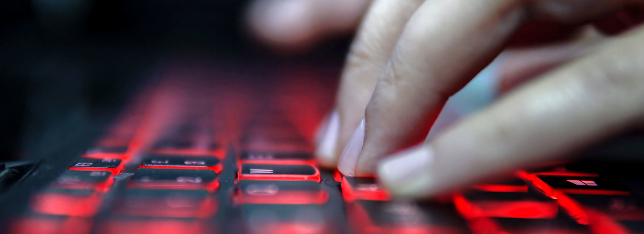 hacker types on a laptop with a red backlit keyboard