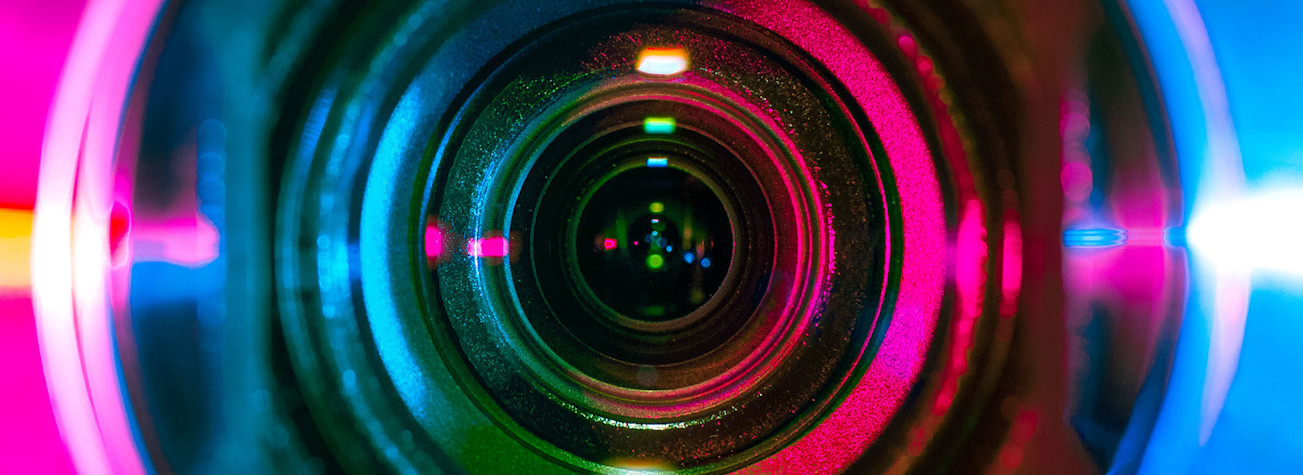 Close-up of video camera lens in which different light colors reflect