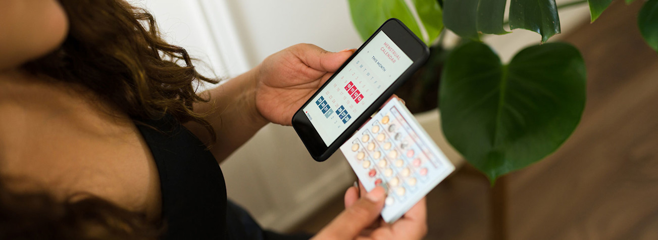 Vrouw met een strip anticonceptiepillen en een smartphone in haar handen