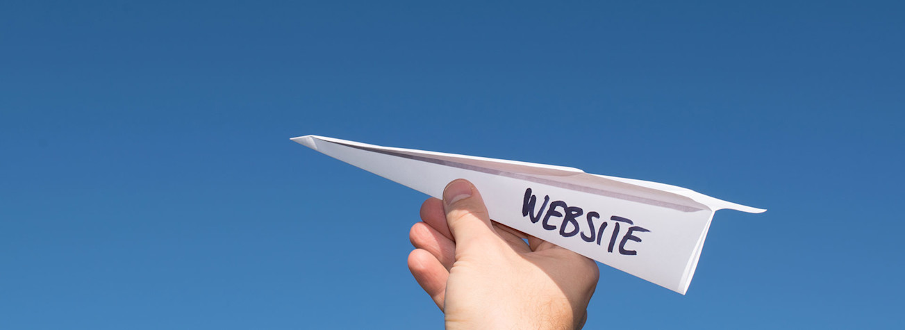 Paper airplane with text 'website' in a hand against a blue sky. (Concept of launching a website. )