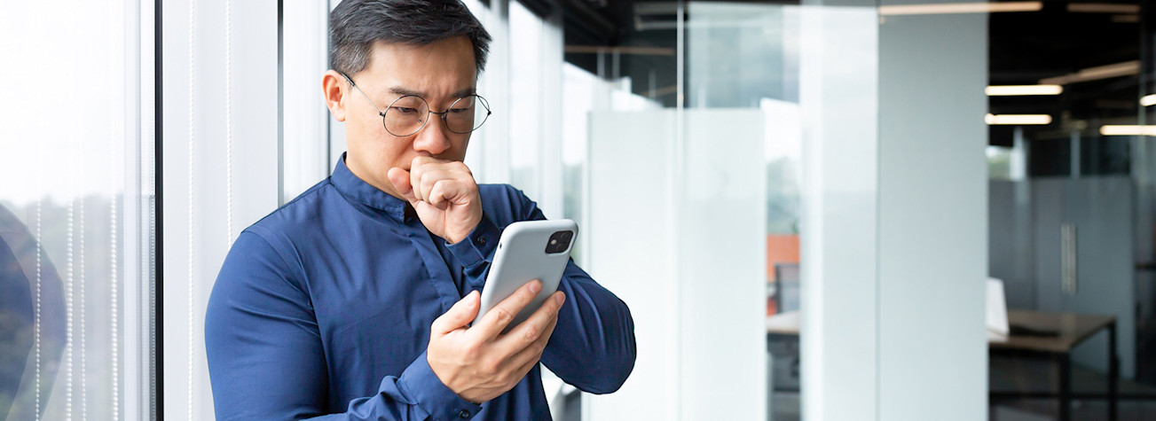 Aziatische man kijkt bezorgd op mobiel want er is fraude gepleegd met zijn domeinnaam