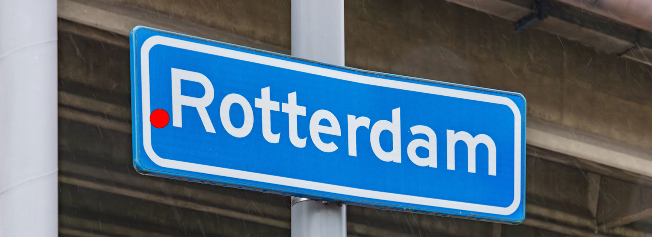 Plaatsnaambord met 'Rotterdam' erop met voor de plaatsnaam een rode punt.