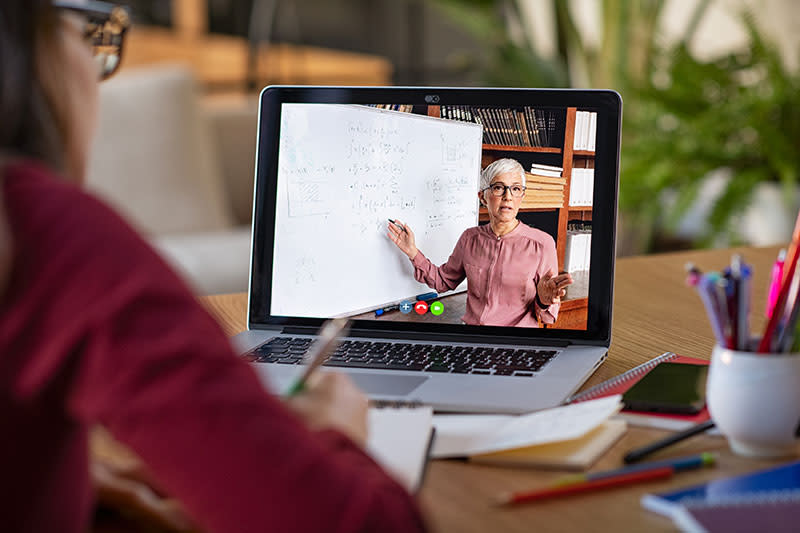 Jonge vrouw maakt aantekeningen terwijl ze naar het computerscherm kijkt en een wiskundeles volgt.