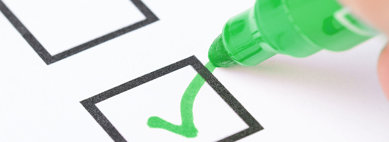 Macro shot of a hand placing a green check mark in the checklist box