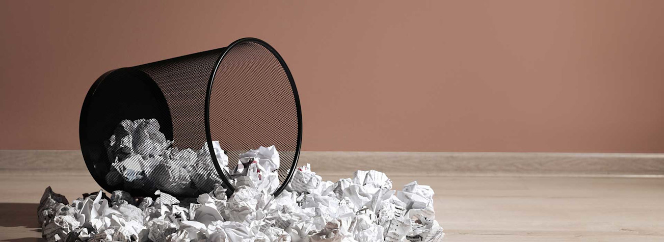 Overturned trash can with wads of paper scattered on the ground around it