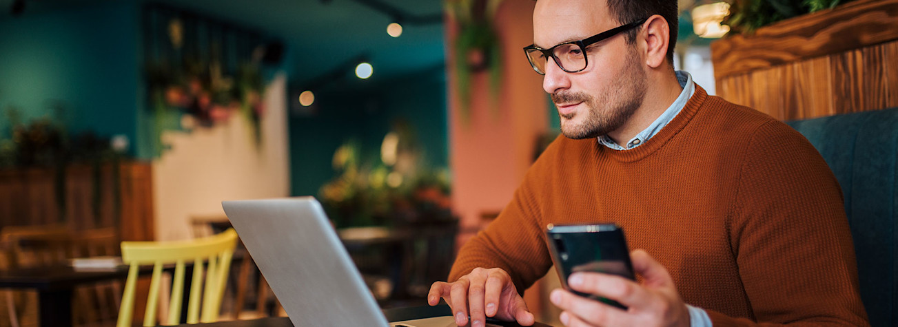 Man werkt op laptop met in zijn linkerhand een smartphone