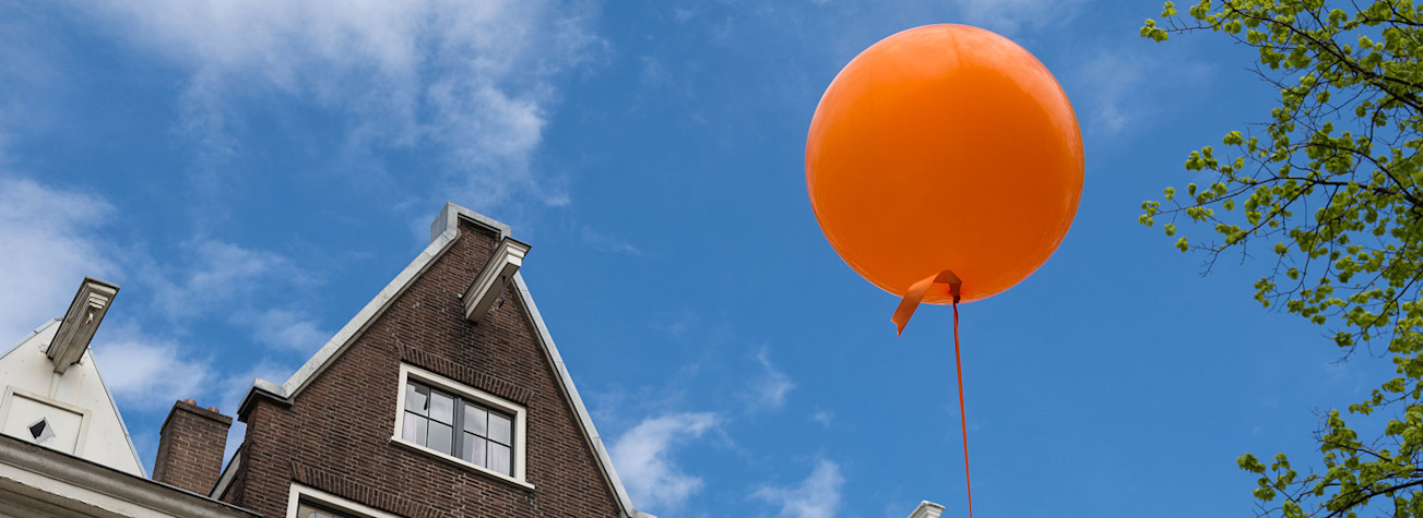 Oranje ballon tegen een blauwe lucht boven Amsterdamse huisjes