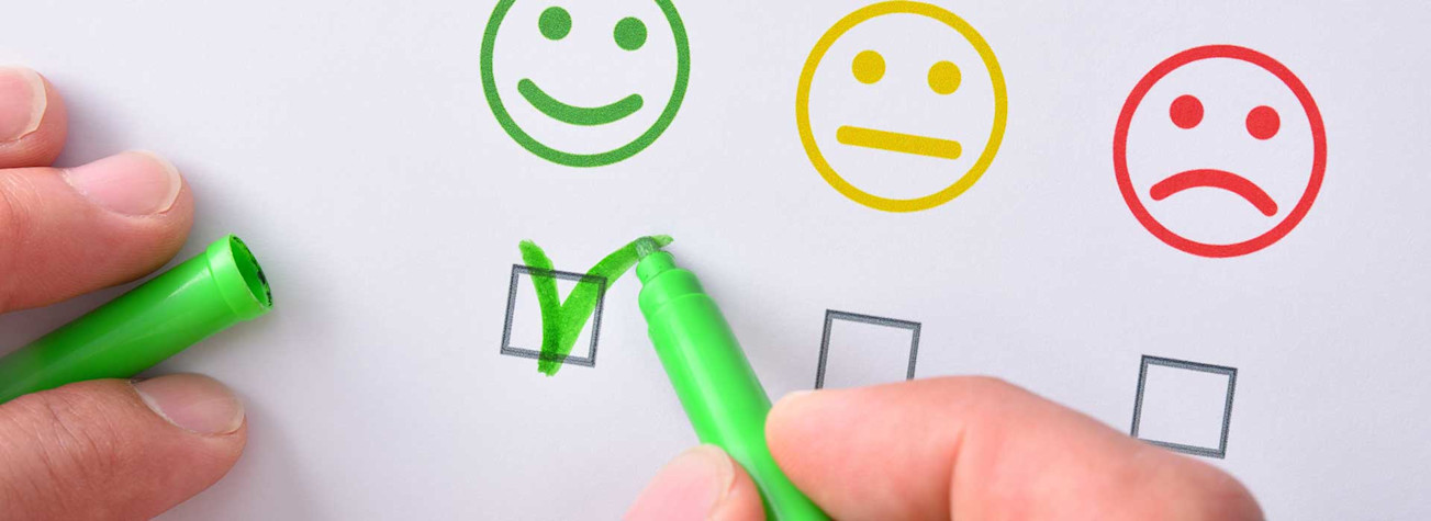 Close-up of a hand using a green felt-tip pen to check a green, satisfied smiley.