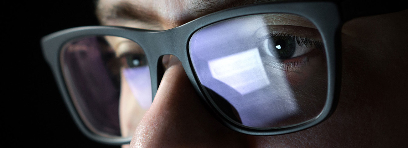 Close up of a face with glasses with the reflection of a computer screen in the glasses