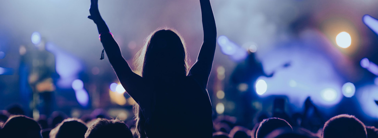 Silhouet van een vrouw met opgeheven handen op een concertzaal.
