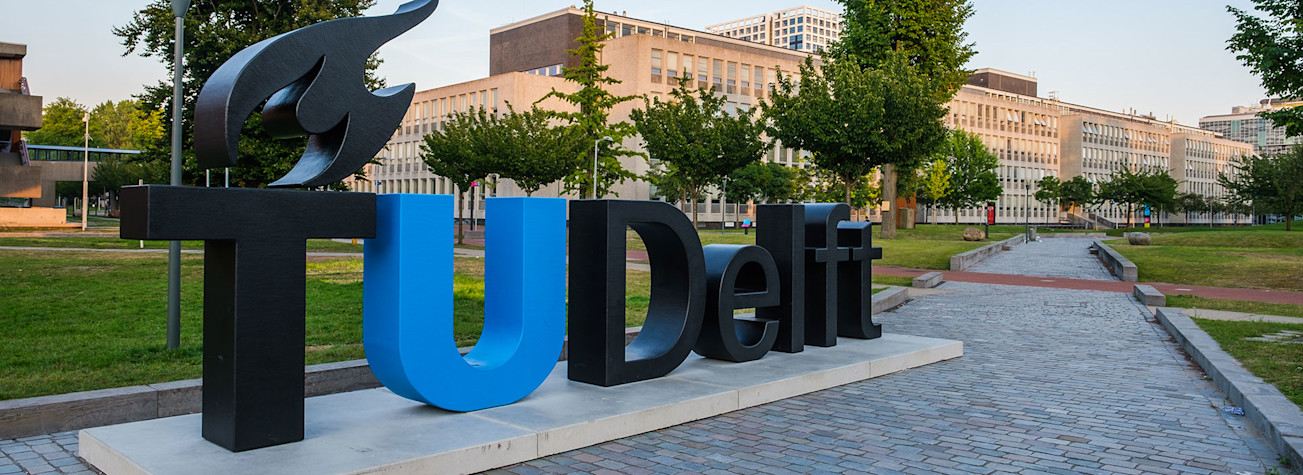 Uitzicht op de campus van de Technische Universiteit Delft, Nederland met het logo van de universiteit in levengrote letters op de voorgrond.