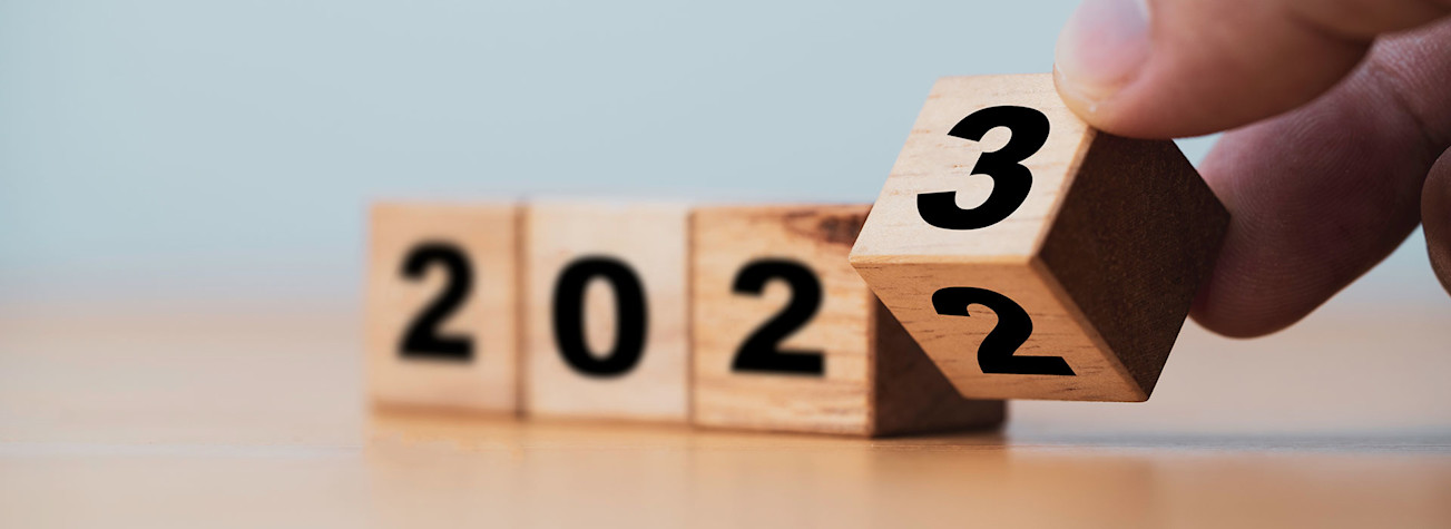 Hand flipping a wooden block from 2 to 3, so that the year 2023 is visible.