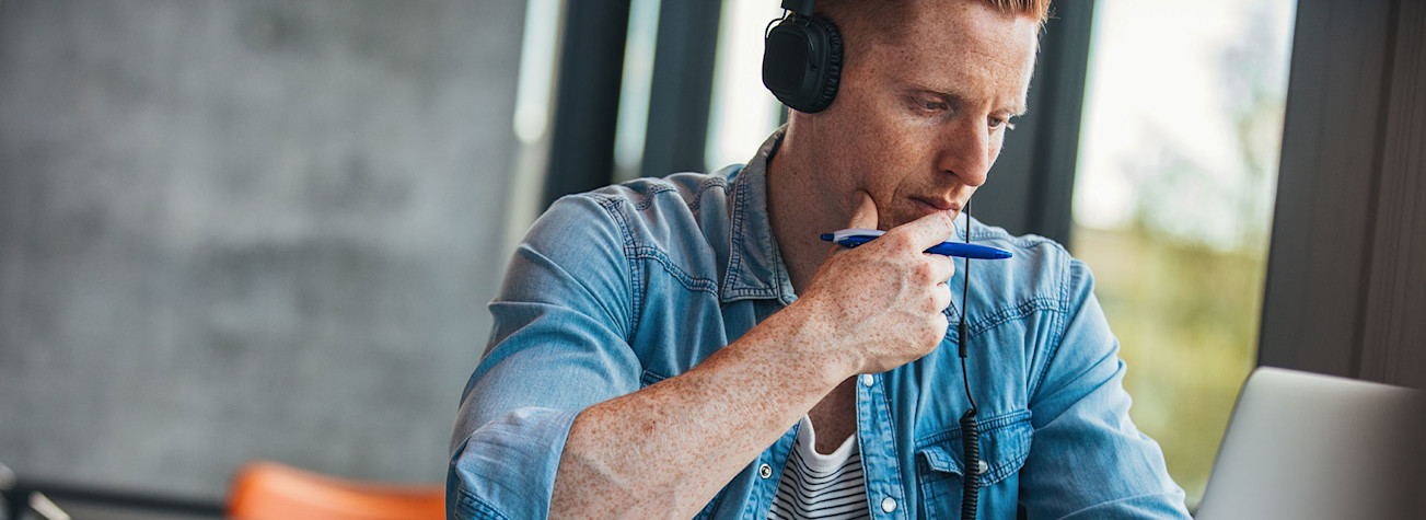 Pensive student with headphones on studying behind a laptop