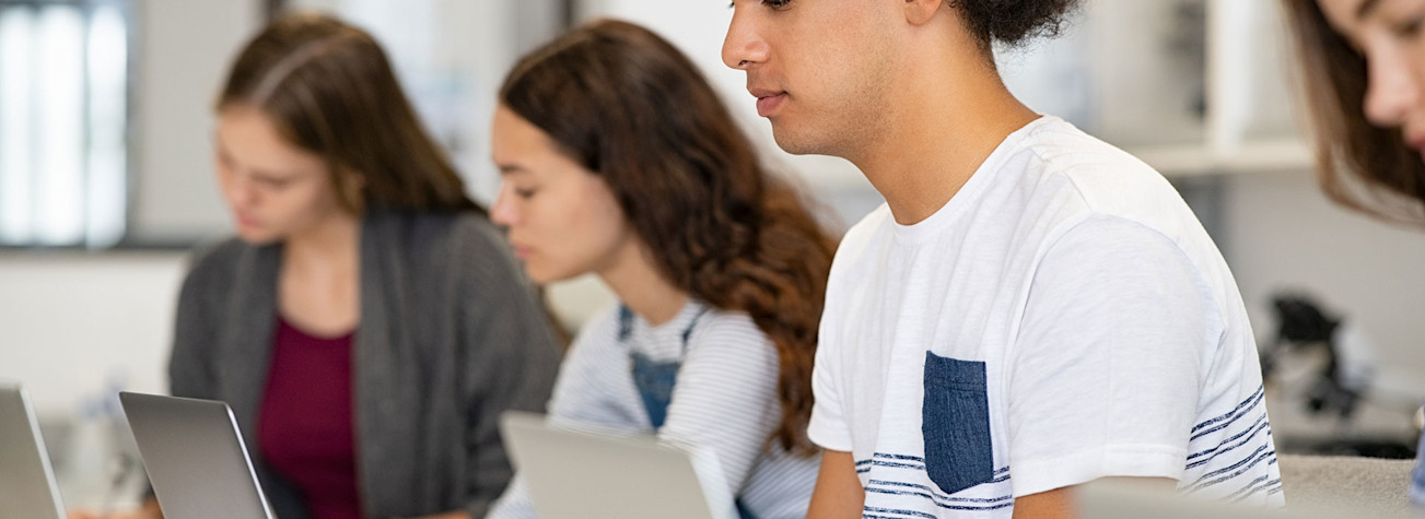 Teenagers working on laptops in a classroom.