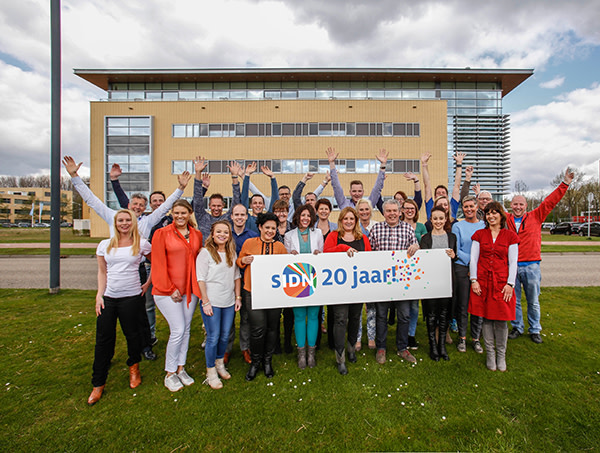 Blije SIDN-collega's voor het pand met een bord '20 jaar SIDN'