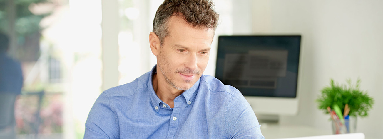 Man sitting behind a desk looks at a laptop screen.