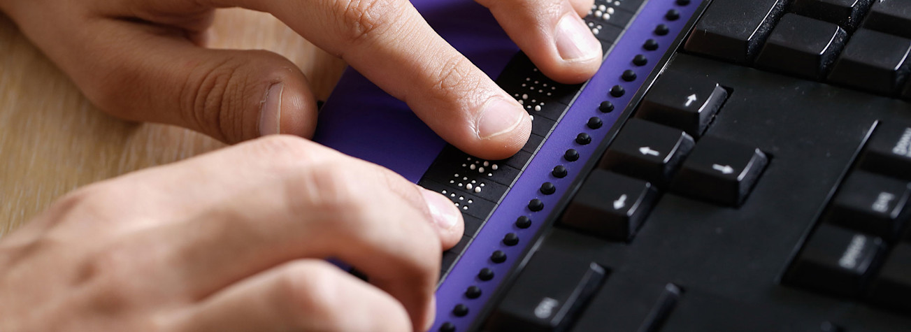 Close-up of hands operating a braille keyboard for the blind