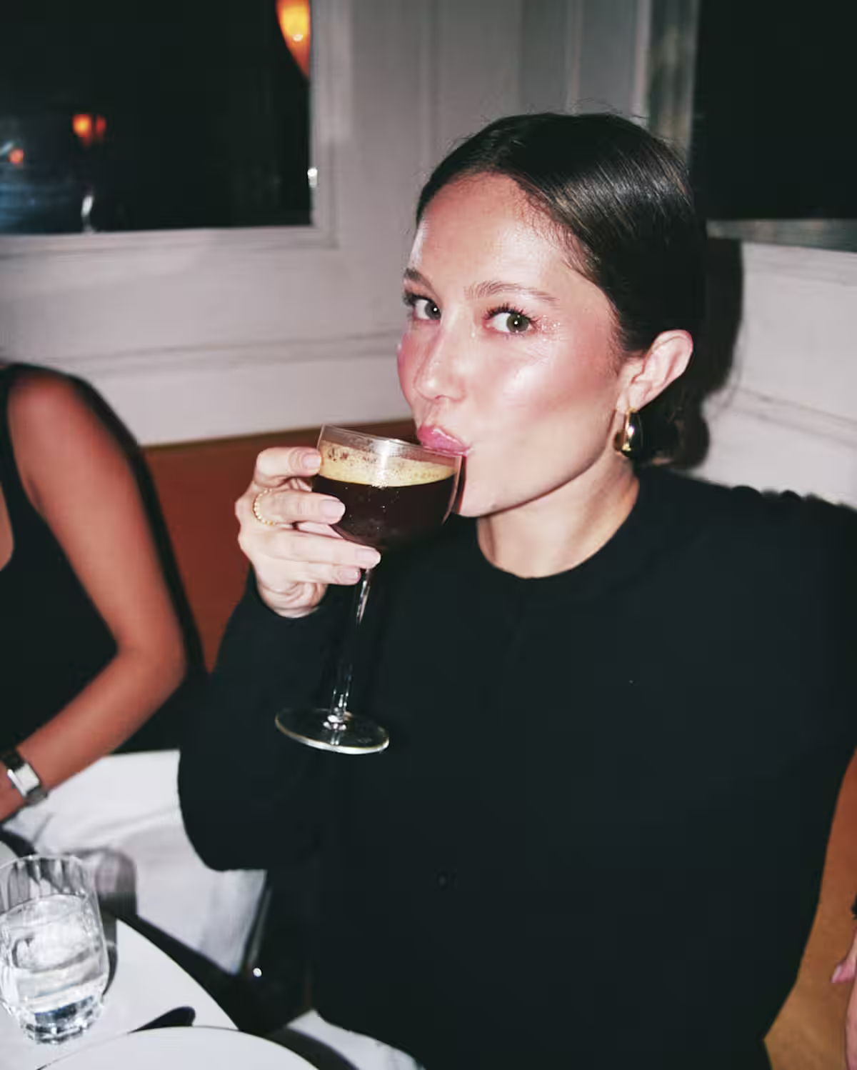 A woman sipping on an Espresso Martini cocktail at a dining table.