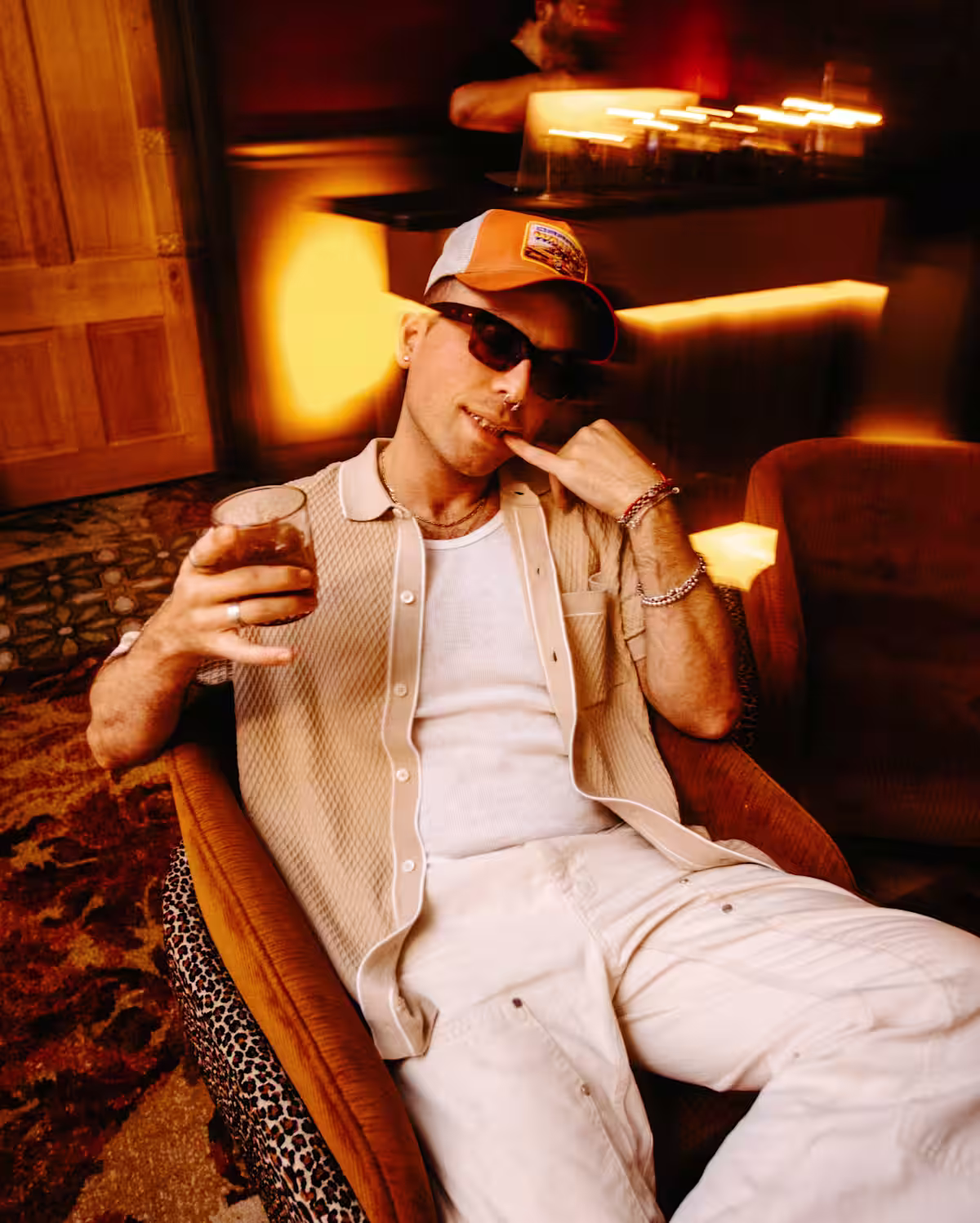 A man wearing sunglasses and a ball cap holding a Coffee Negroni cocktail while lounging in a bar setting.