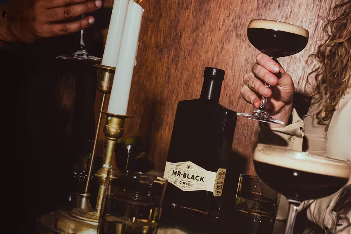 Three espresso martinis on a platter being served to people sitting at a table