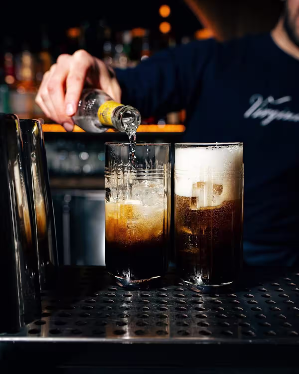 A bartender pouring tonic water into a highball glass filled with ice and Mr Black Coffee Liqueur