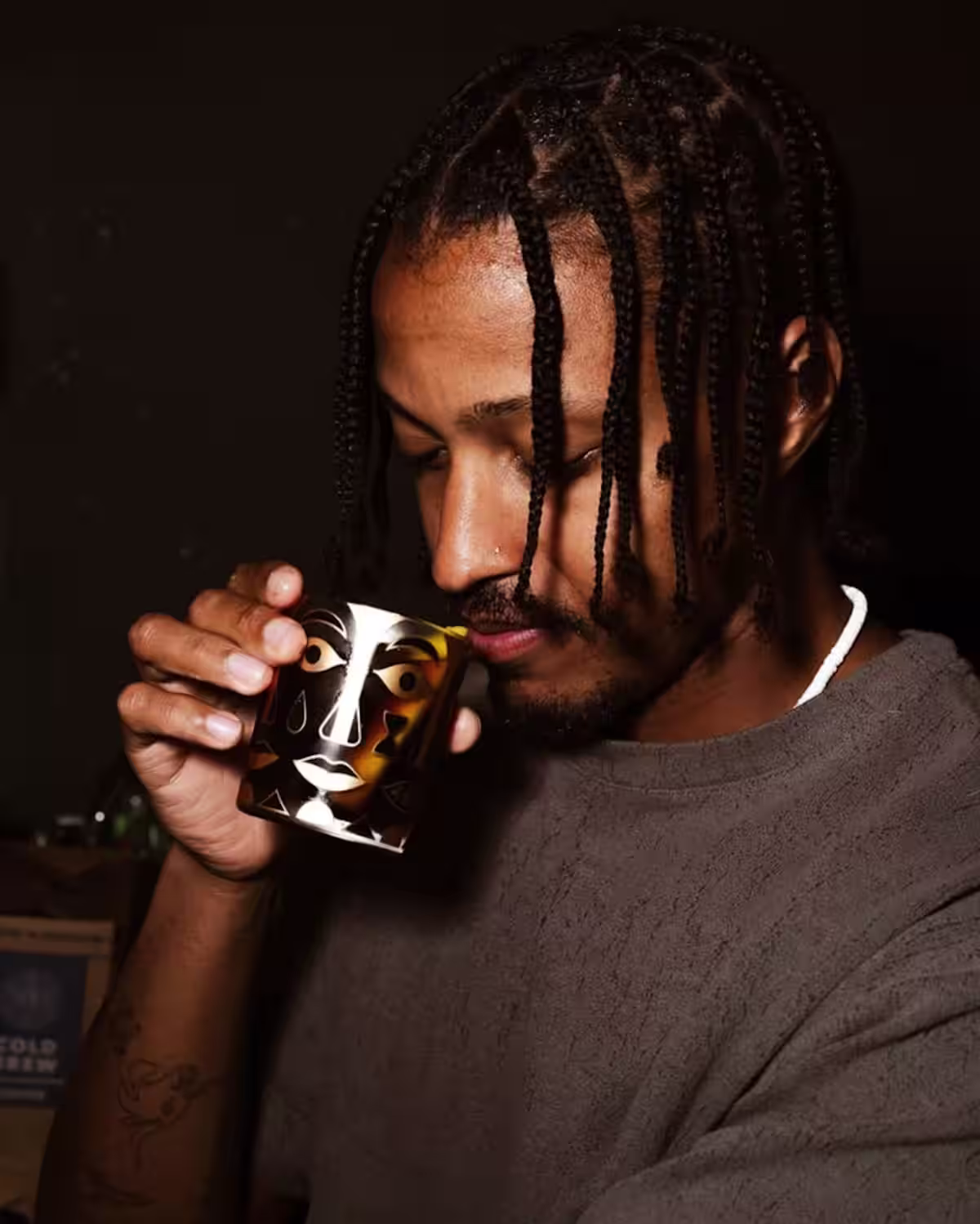 A man drinking a Cold Fashioned cocktail from a rocks glass with a retro face design.