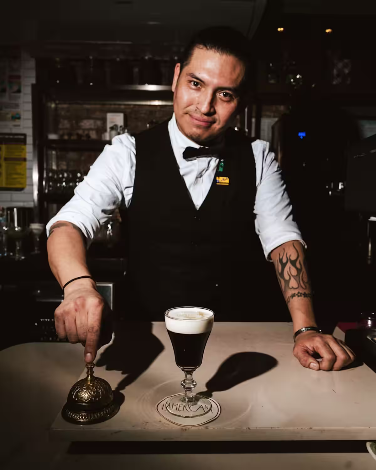 A bartender ready to press an antique brass service bell with a Mr Black Cold Brew Irish Coffee cocktail ready to serve