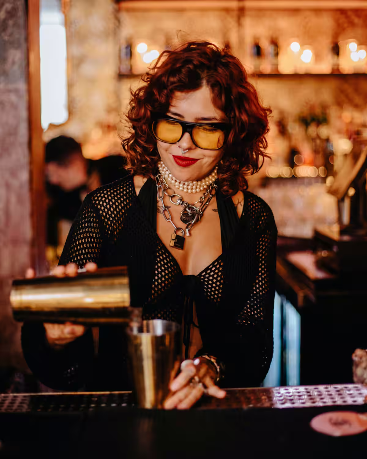 A woman bartender pouring a cocktail shaker at the bar counter.