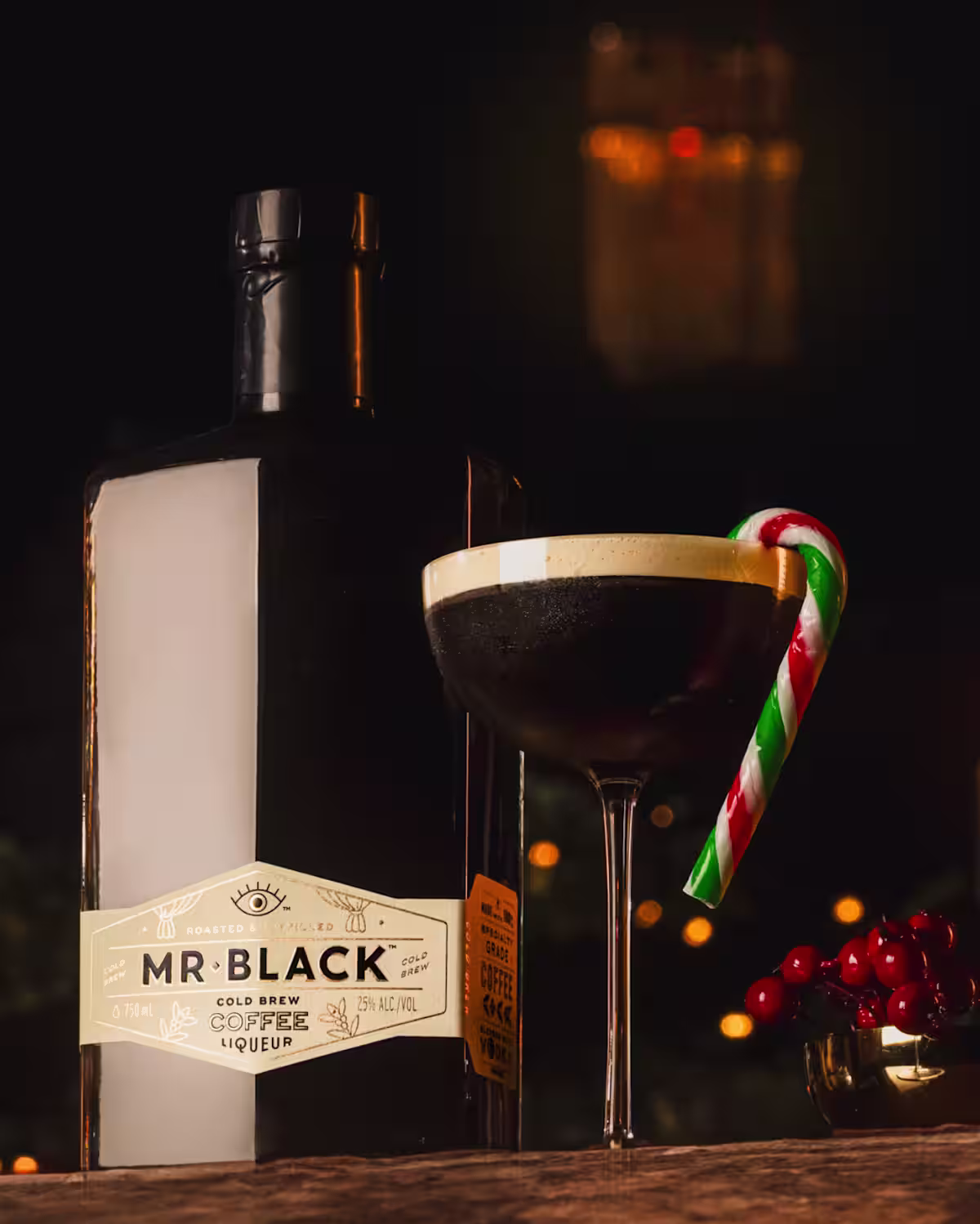 An Espresso Mint-tini cocktail with a green, red, and white striped candy cane as garnish next to a bottle of Mr Black Coffee Liqueur