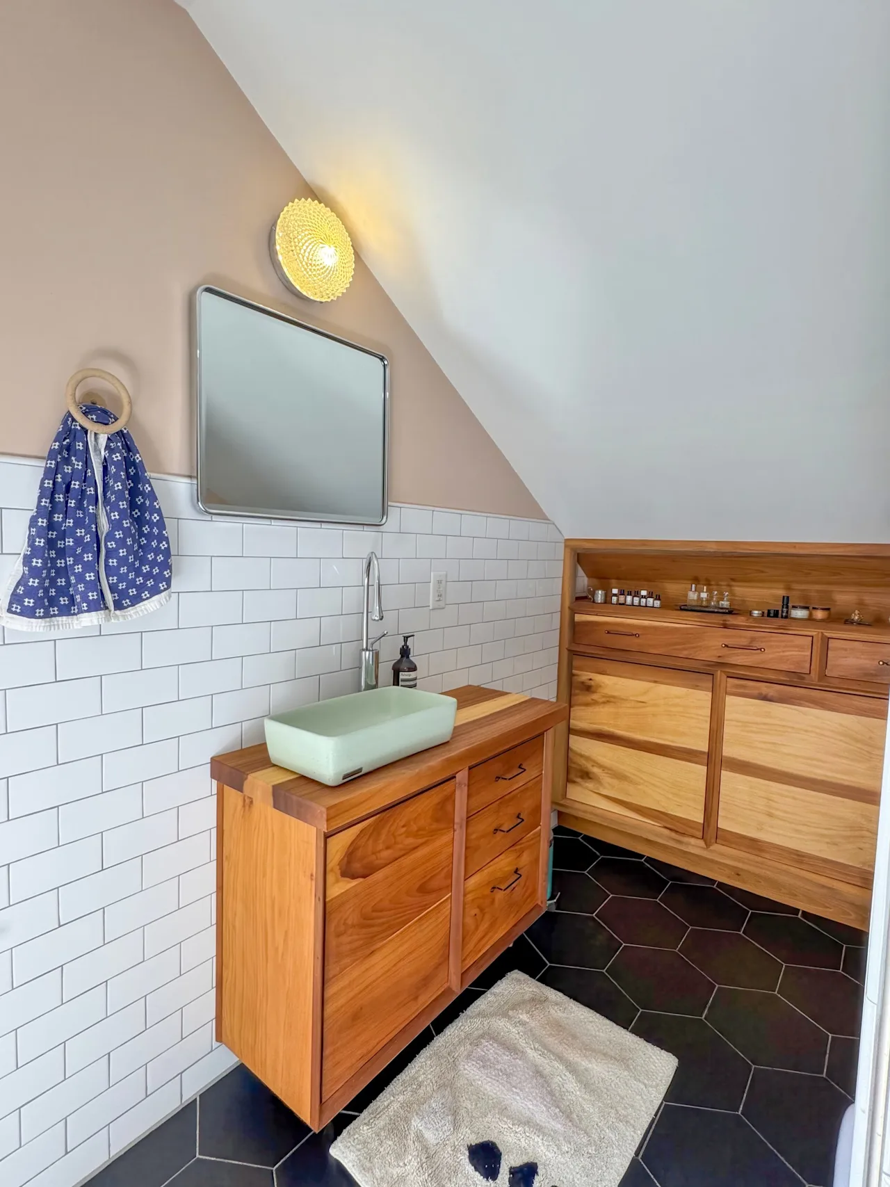 Bathroom corner with a wood vanity, a green vessel sink, white subway tile, and a sloped ceiling.