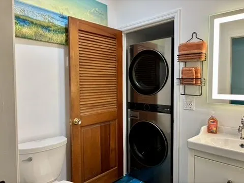 Bathroom with a stacked washer and dryer behind a louvered door, a white subway-tile shower, and a lit vanity mirror.