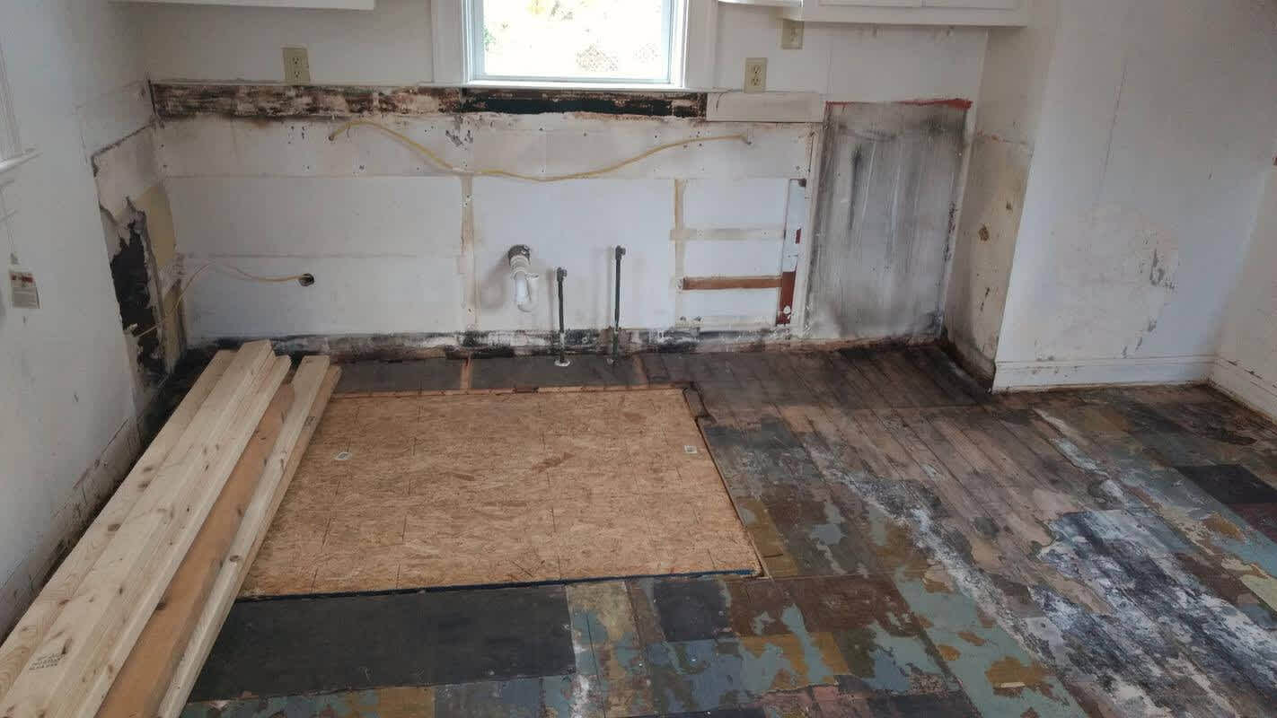 Kitchen area pre-reno with exposed plywood, water staining, and cabinets removed