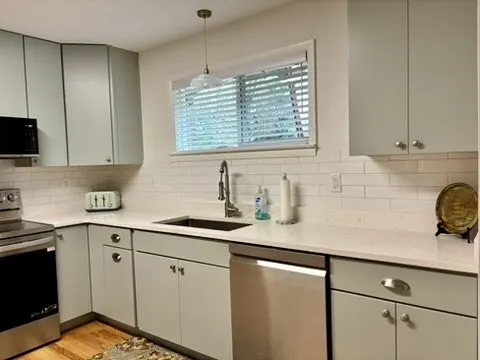Updated kitchen with pale-green cabinets, white subway-tile backsplash, quartz counters, and stainless appliances.