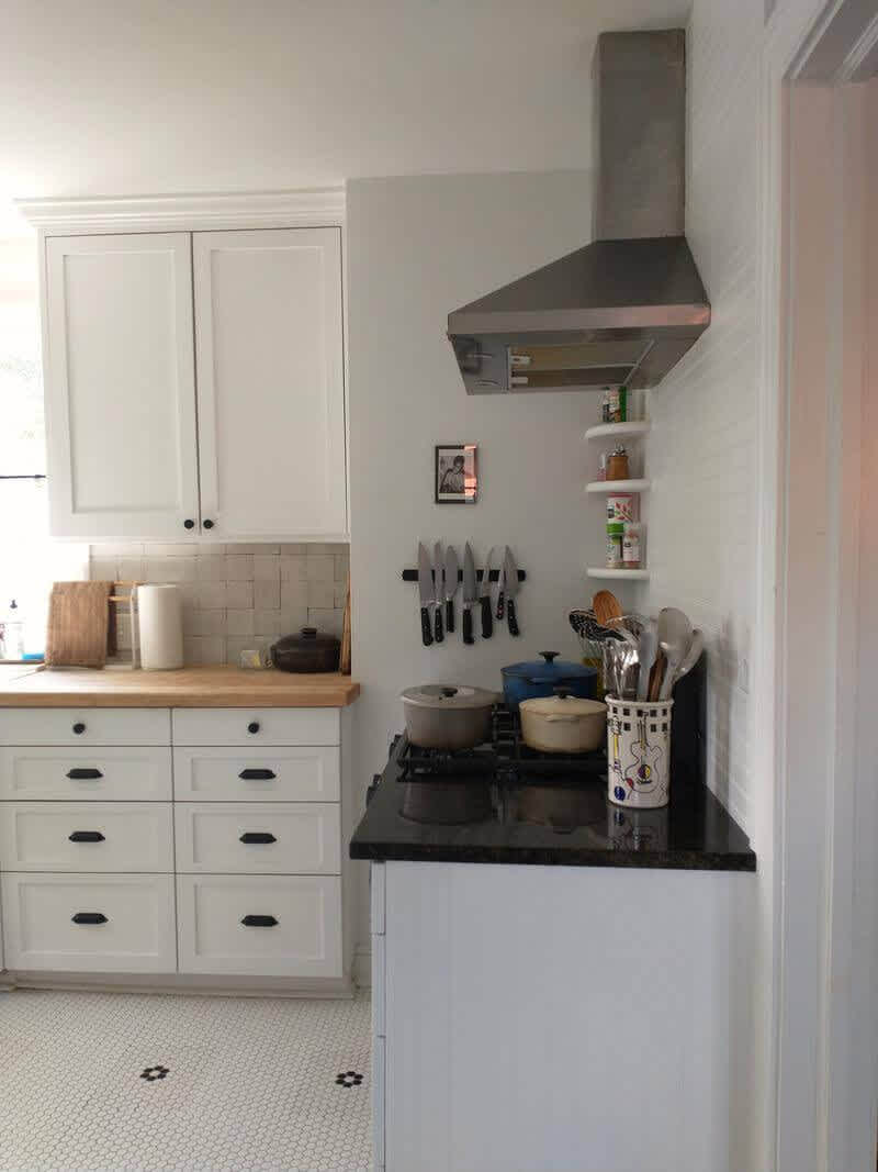A bright white kitchen with a hood, range and cabinet with drawers.