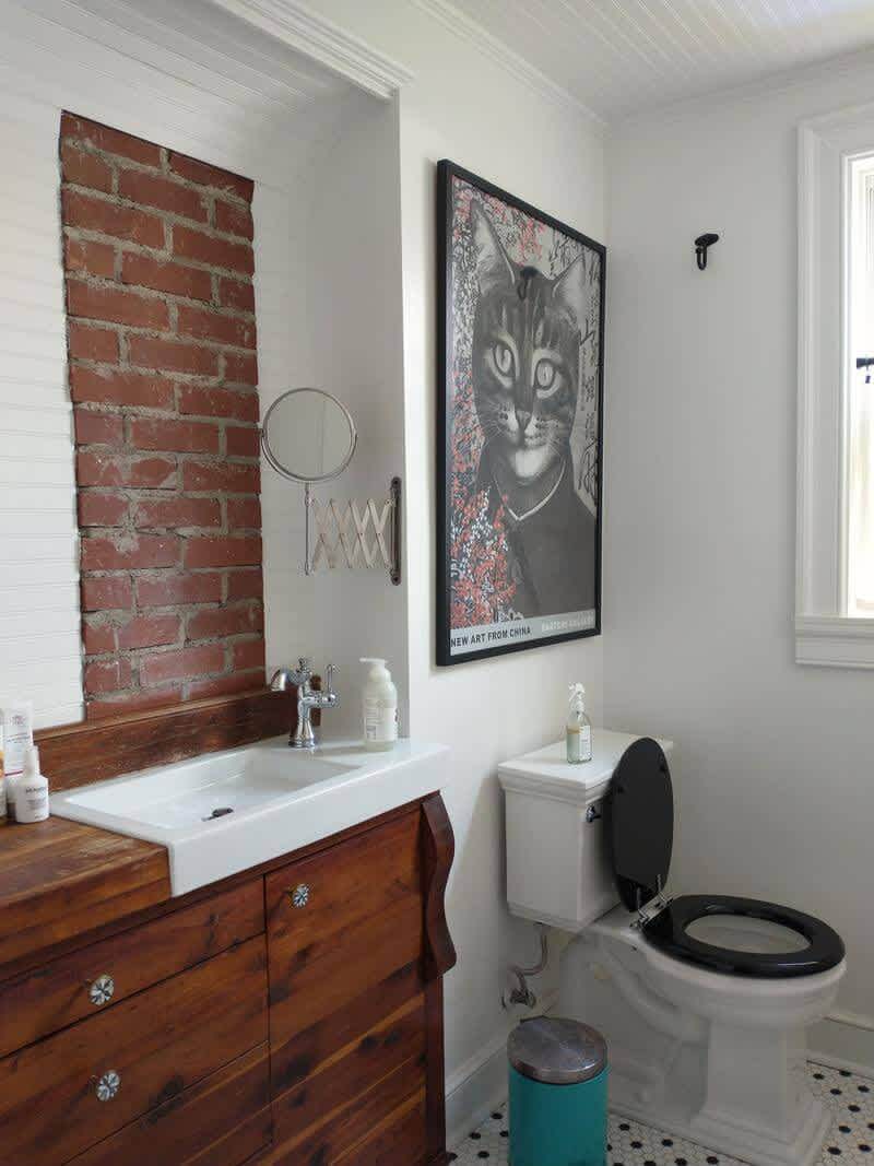 A white sink with an extending mirror, a black and white tile floor, and toilet with wall art