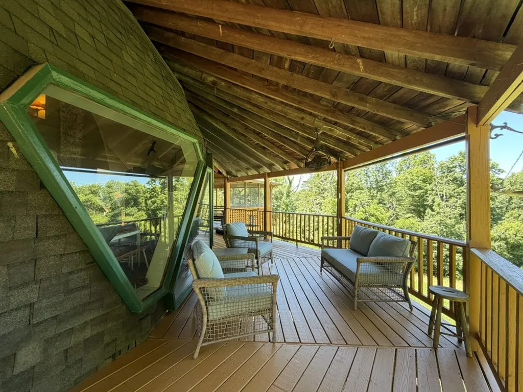 Wraparound porch with an angular green-framed window, wicker seating, and stone walls beneath a wood roof.