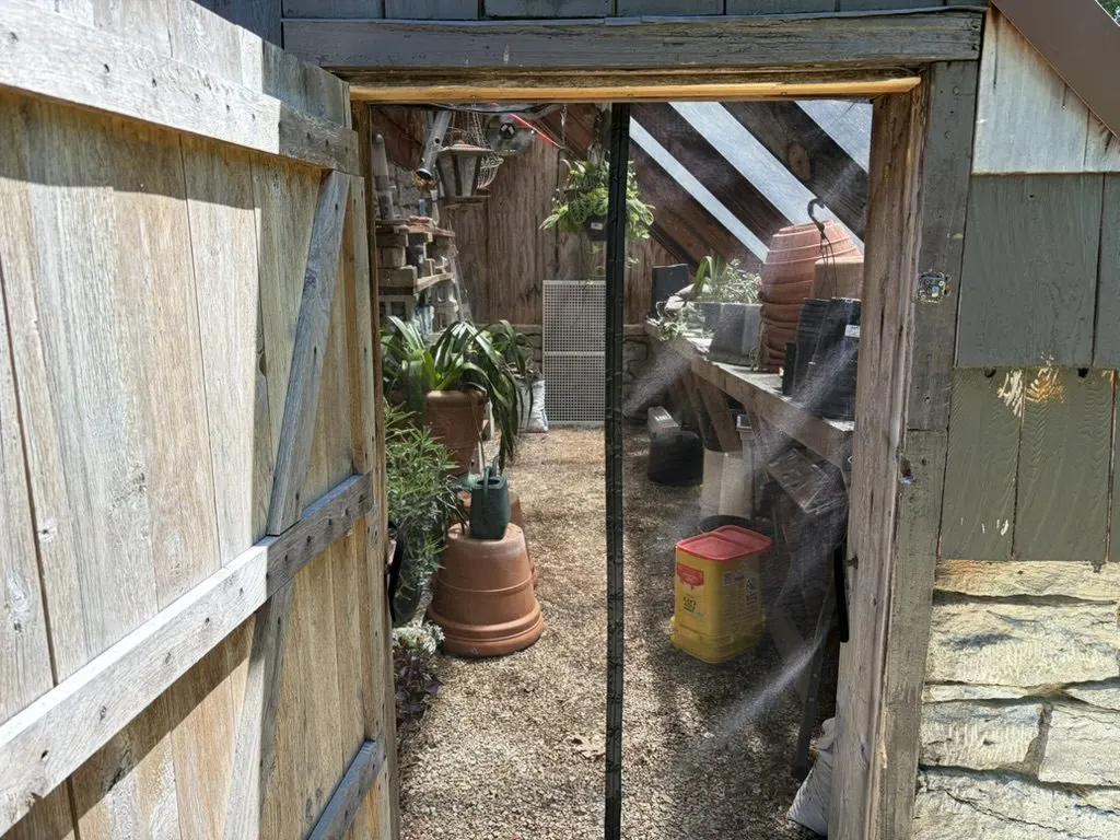 Reclaimed-wood barn doorway opening onto the sunlit greenhouse potting area.