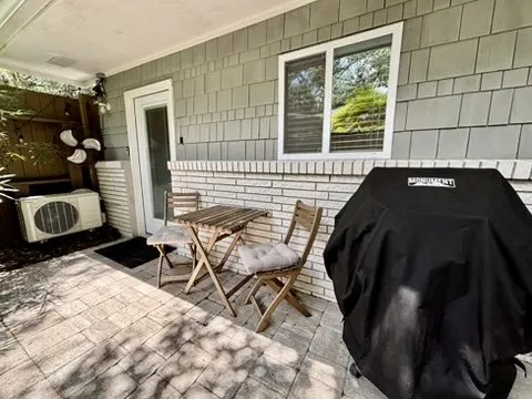 Outdoor patio with shingled walls, a bistro table and chairs, a grill, and a window-unit air conditioner.