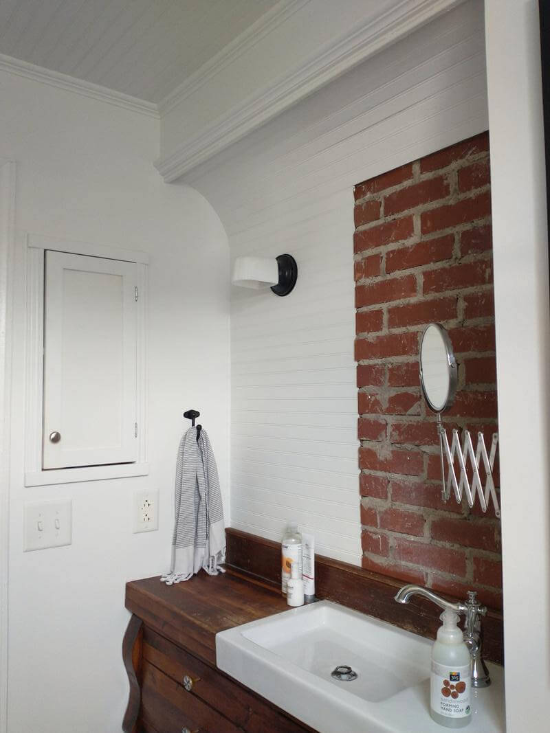 Wooden counter top with a modern white sink and an exposed brick backsplash
