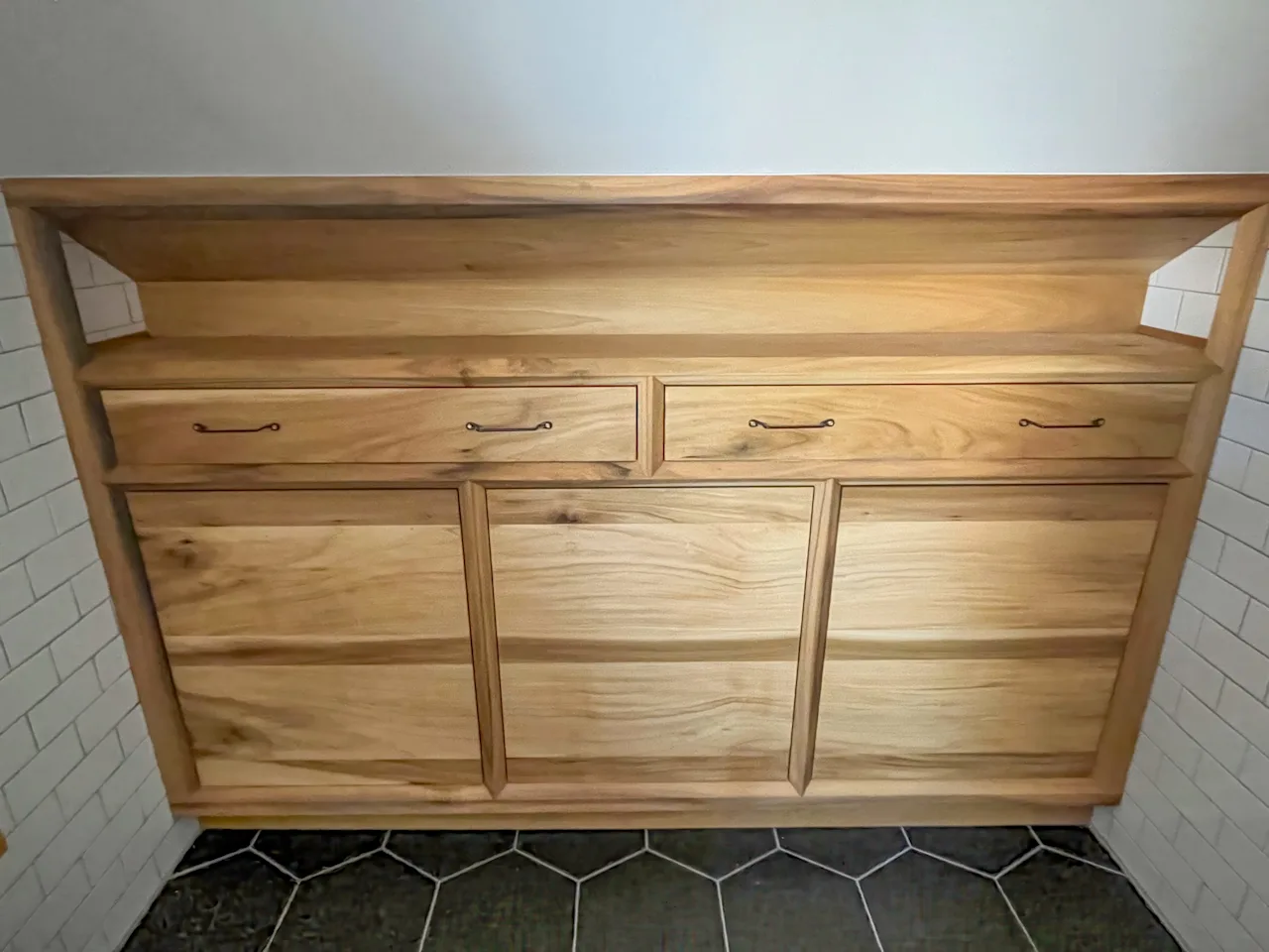 Close-up of the custom wood vanity with a butcher-block top and inset drawers on a hexagon-tile floor.